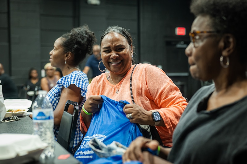 A woman laughs while holding a tote bag at an event.