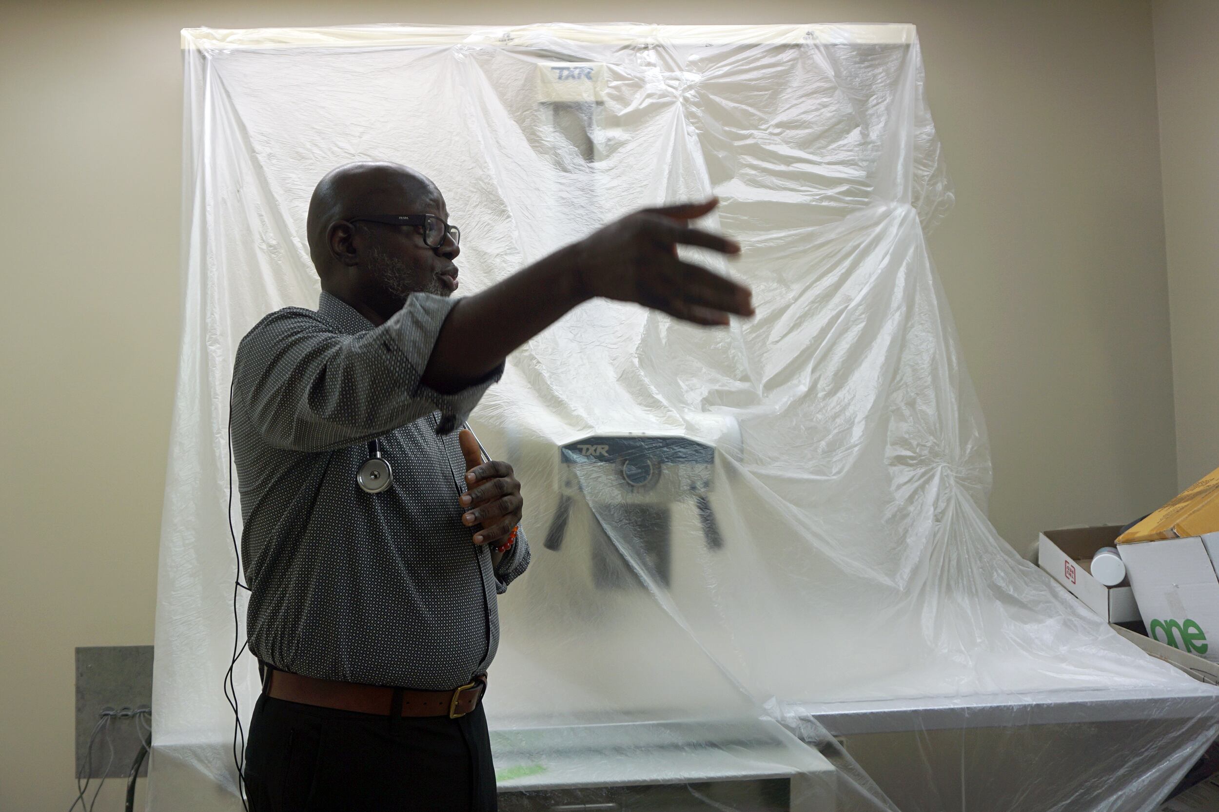 A photograph of a Black man wearing a dress shirt and a stethoscope around his neck speaks from inside of a laboratory.