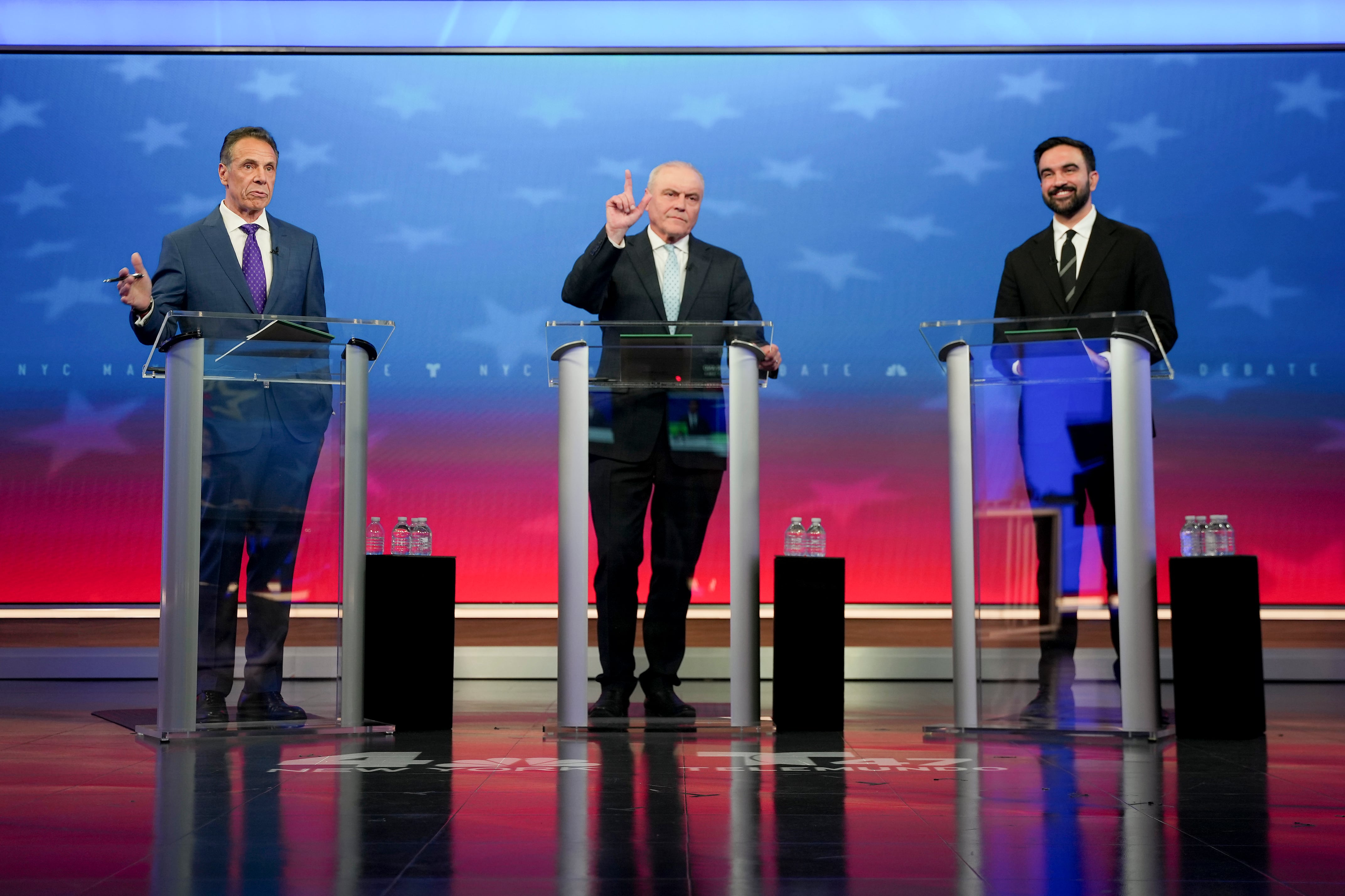 New York City mayoral candidates Andrew Cuomo, Curtis Sliwa, and Zohran Mamdani stand at podiums on the debate stage.