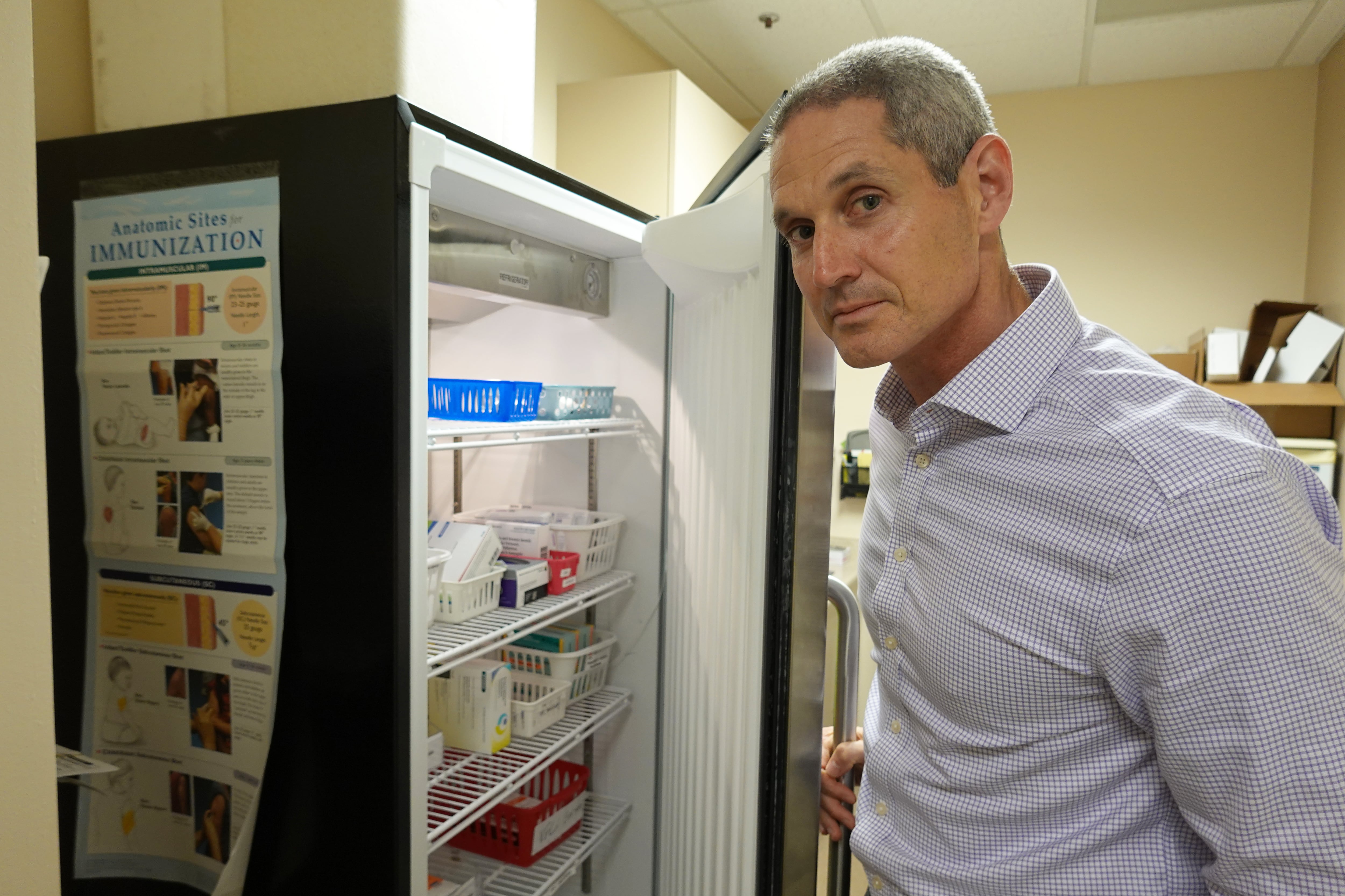 A pediatrician looks at vaccine vials in a refrigerator at his office.