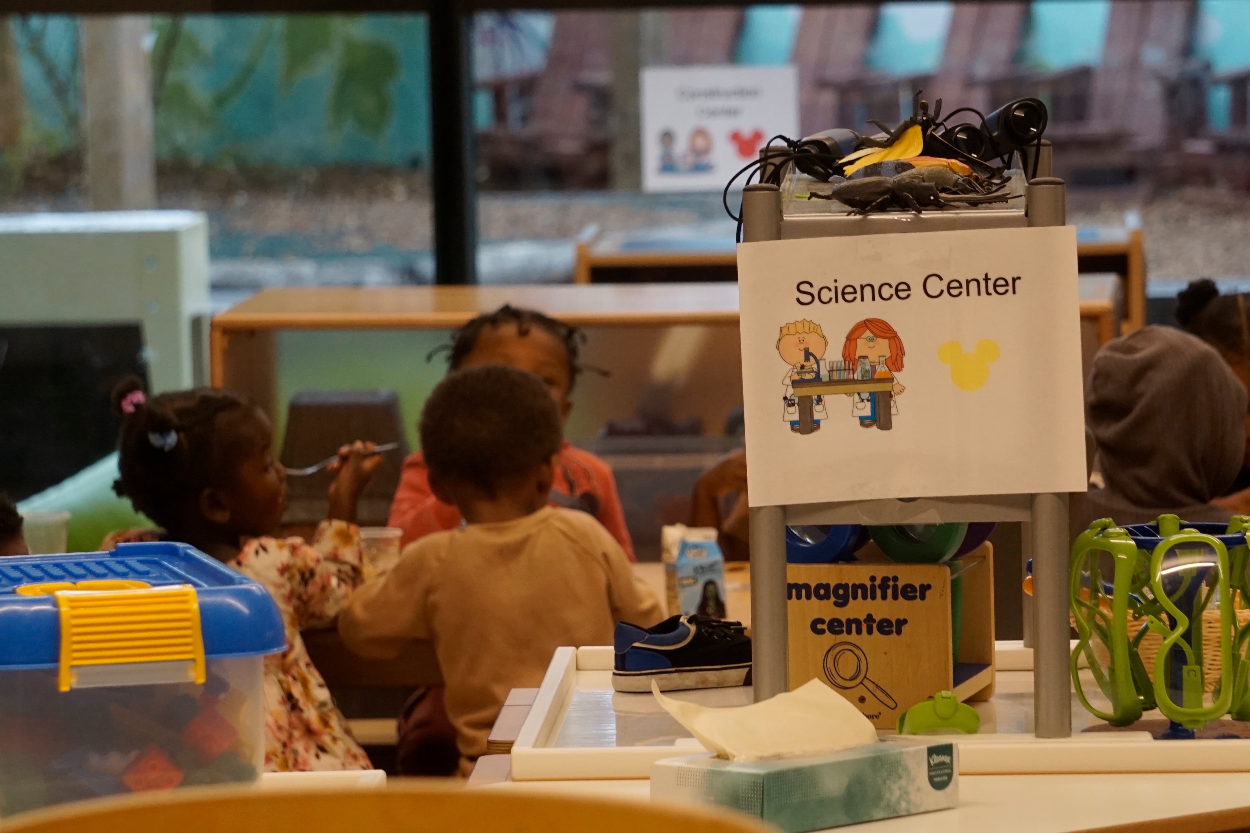 Young children sit at a table in a classroom behind a science station.