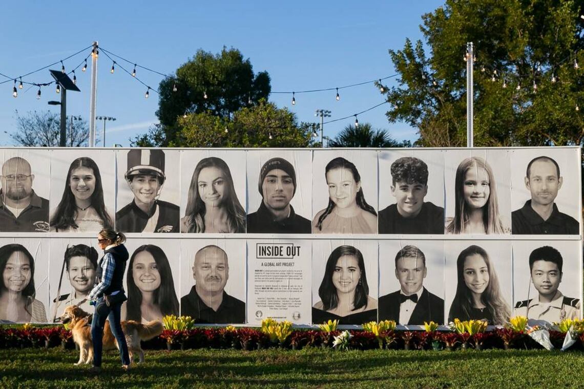 A woman with a service dog walks past a memorial showing photos of those who died in the shooting at Marjory Stoneman Douglas High School.