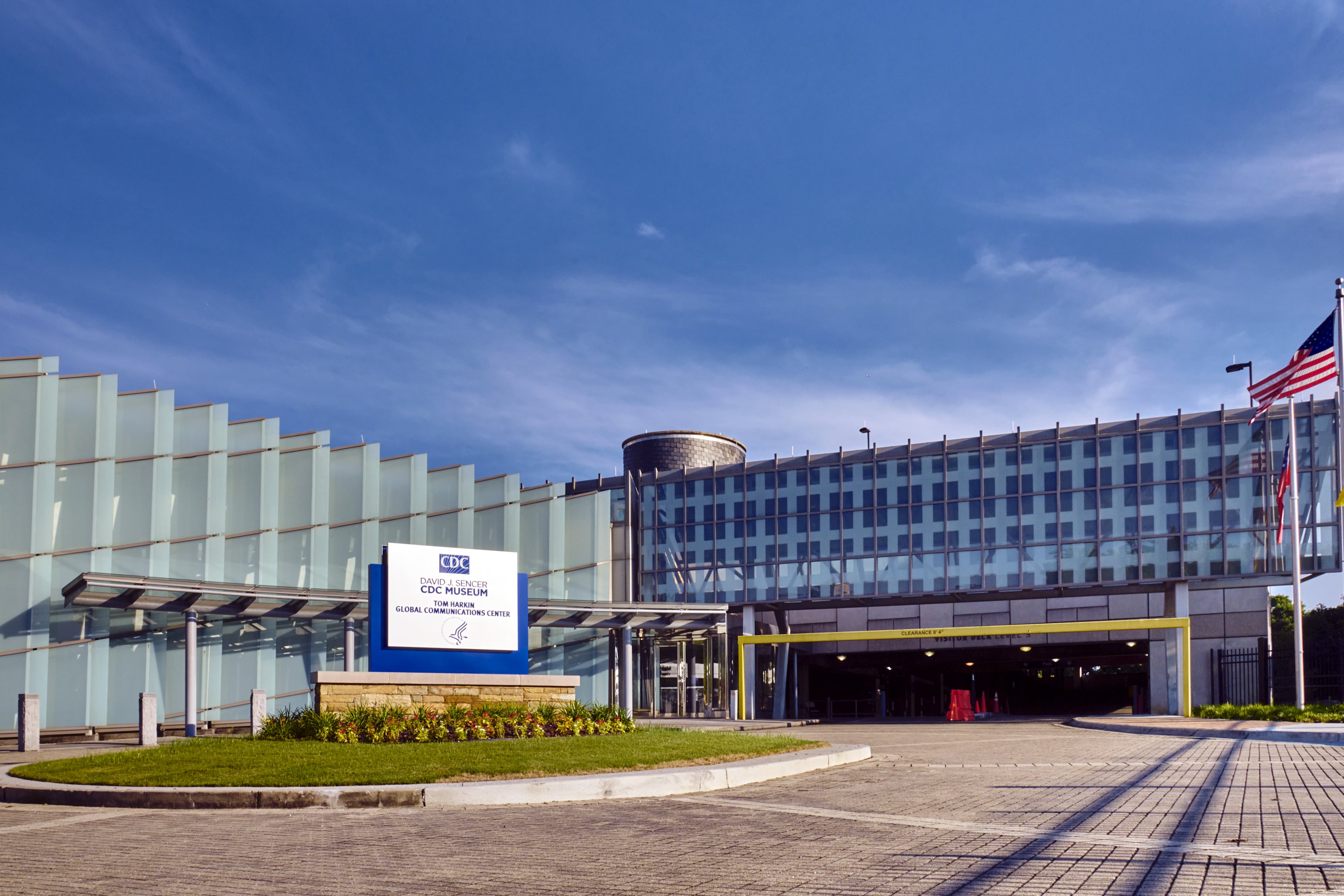 The front entrance of a large building with a sign in the foreground on a sunny day.