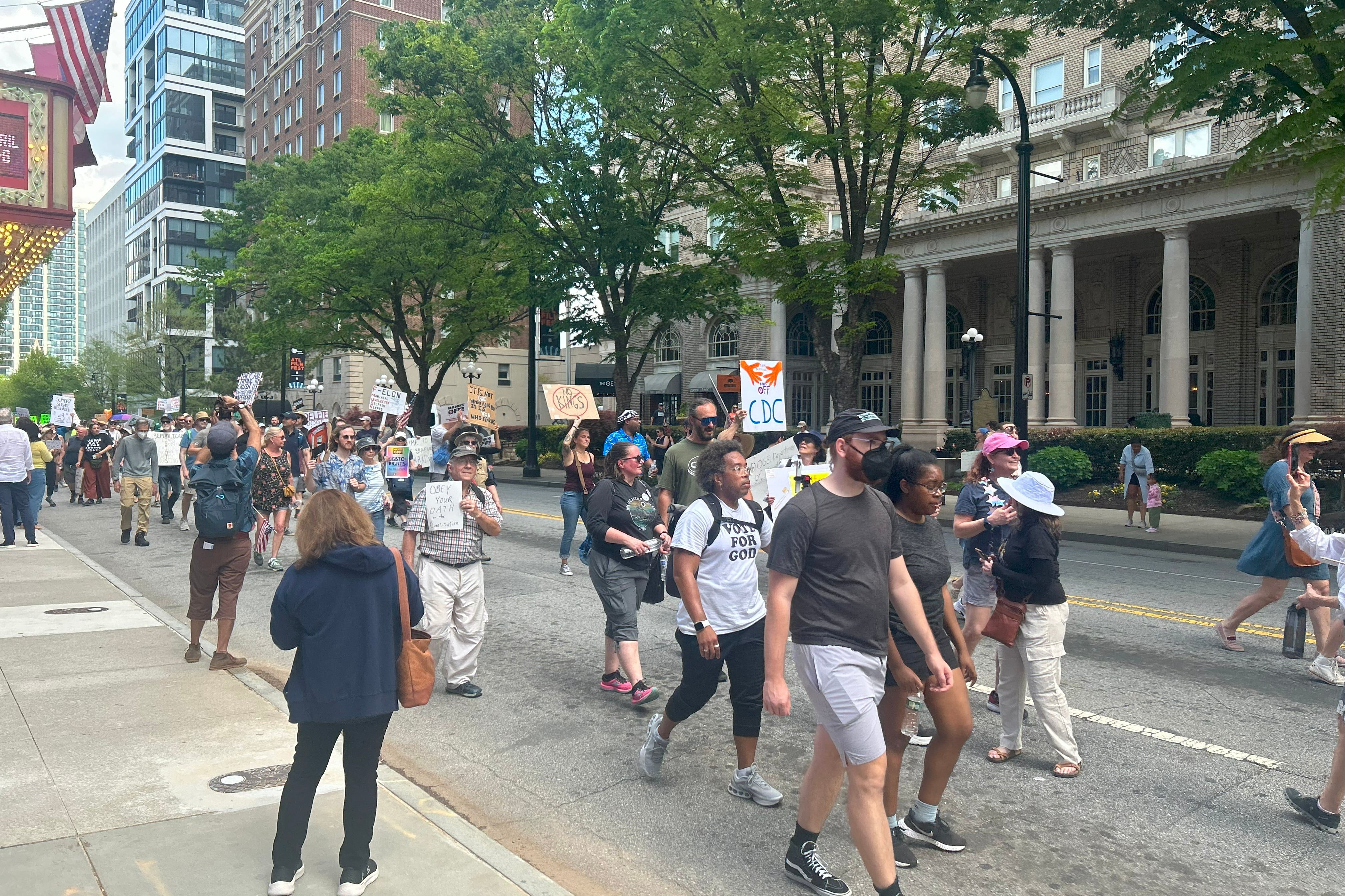 People march down a street holding protest signs.