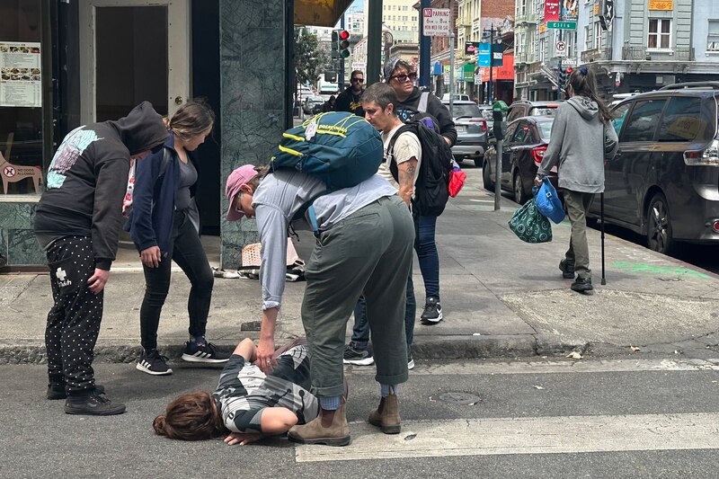 A community health worker helps a homeless woman writing on the ground.
