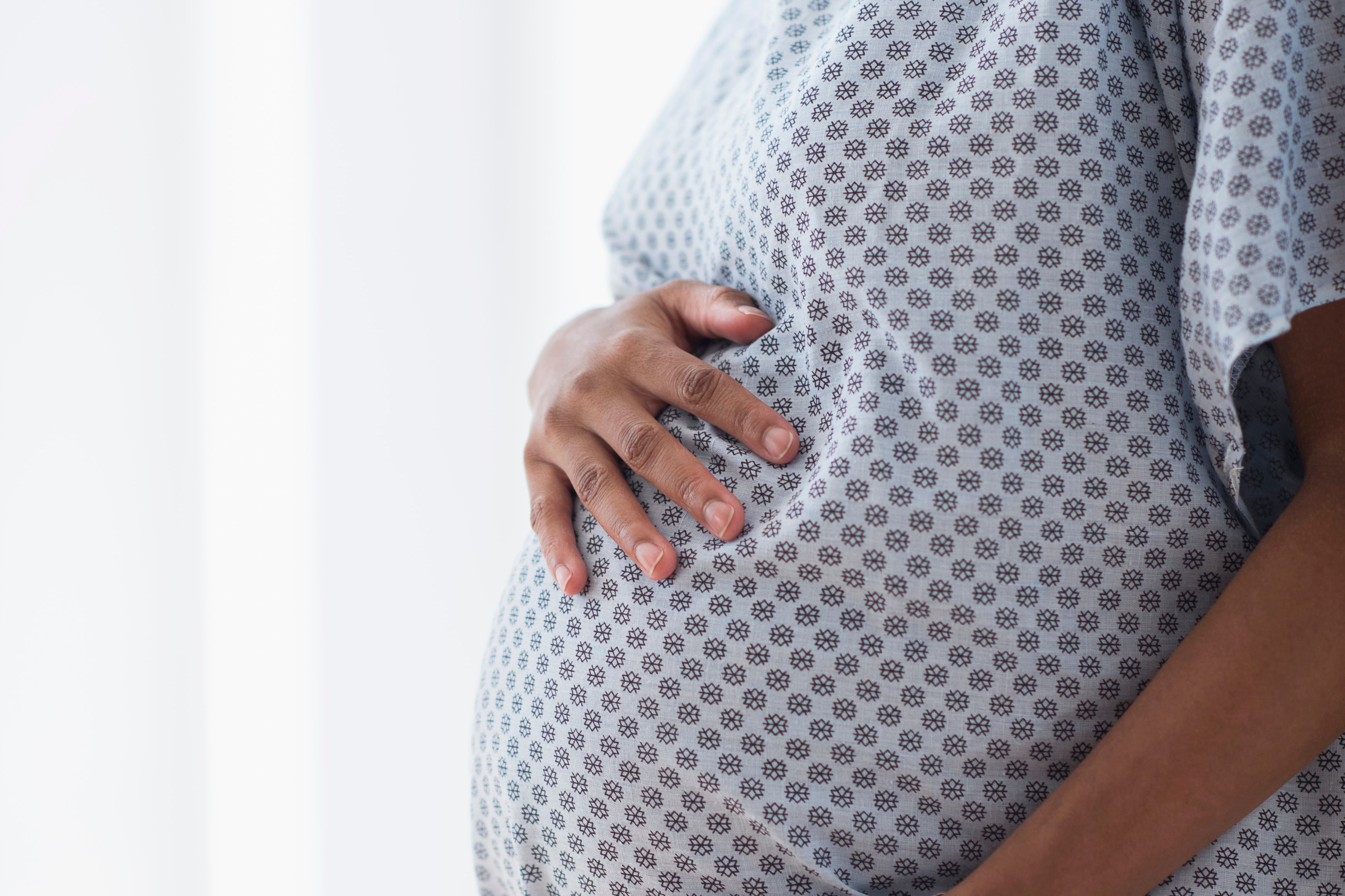 Pregnant African American mother holding her belly in hospital gown