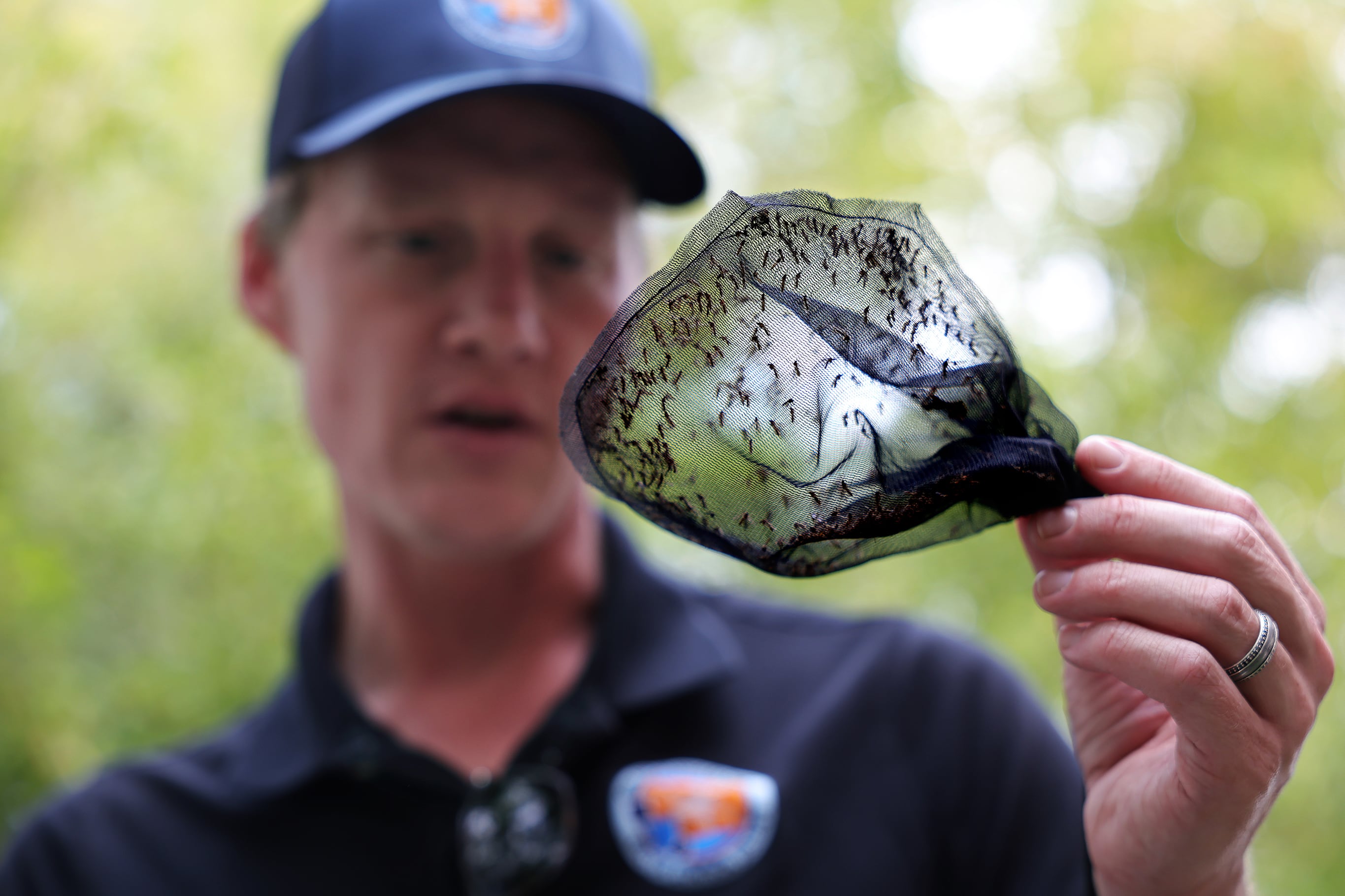 An LA County Vector Control man collects mosquitos in traps outside with greenery in the background.