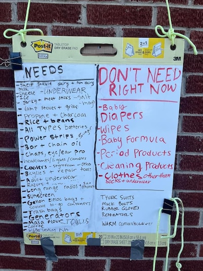 A white board has a list of needs and "don't need right now" items at a relief distribution center.