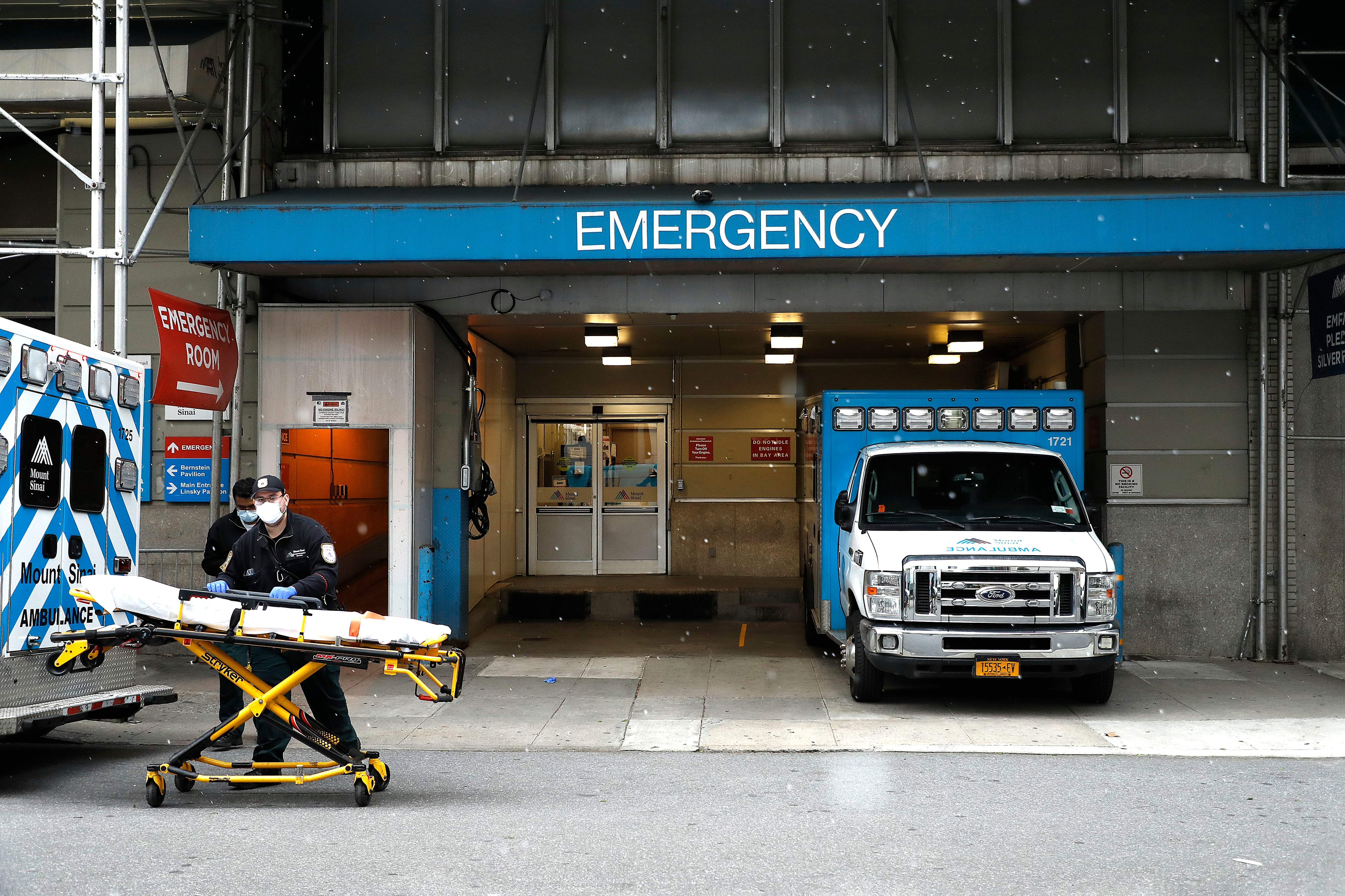 An emergency medical technician moves a gurney near ambulances outside a hospital emergency room.