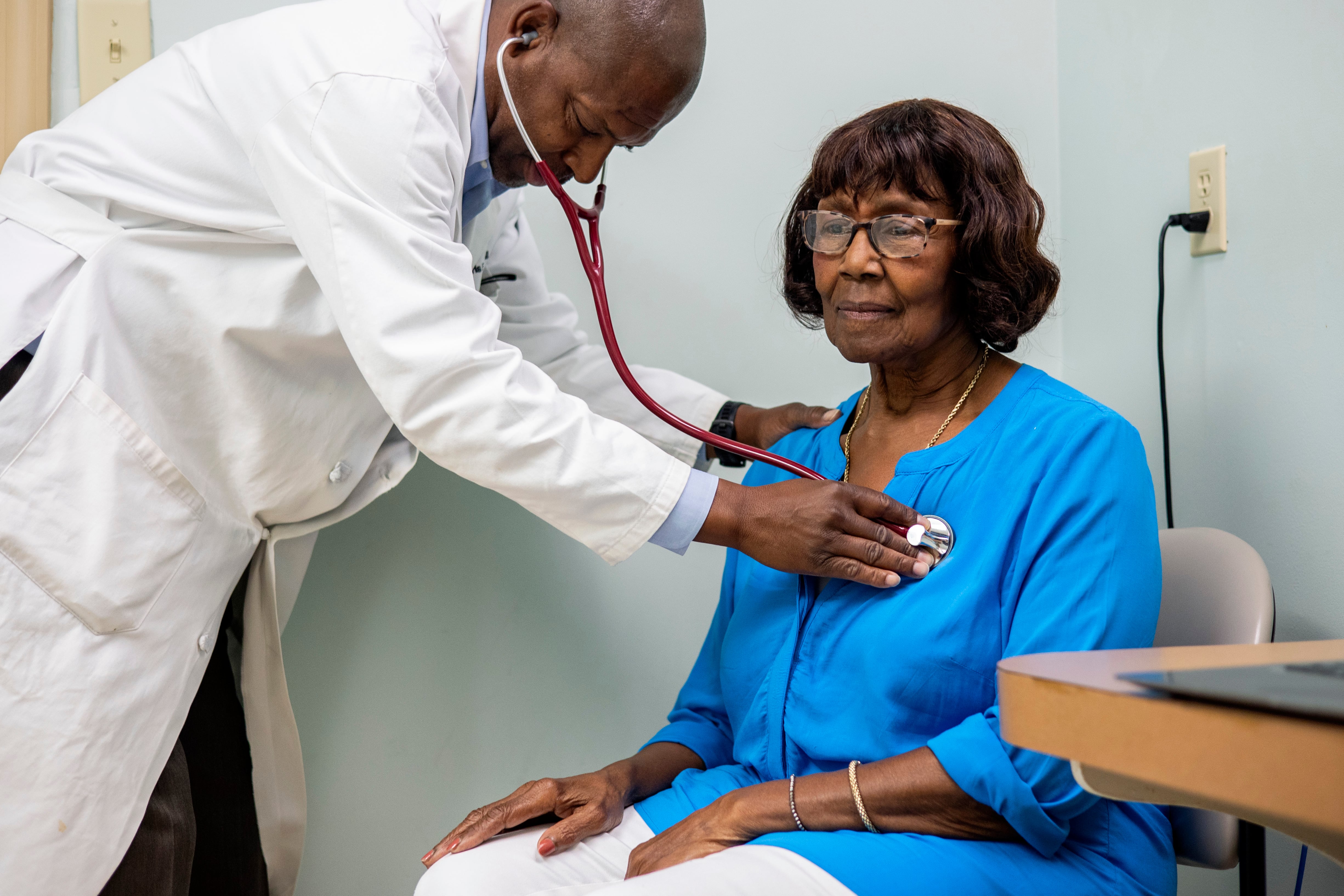Dr. Morris Brown listens to a woman's heartbeat with a stethoscope in an exam room at his office.