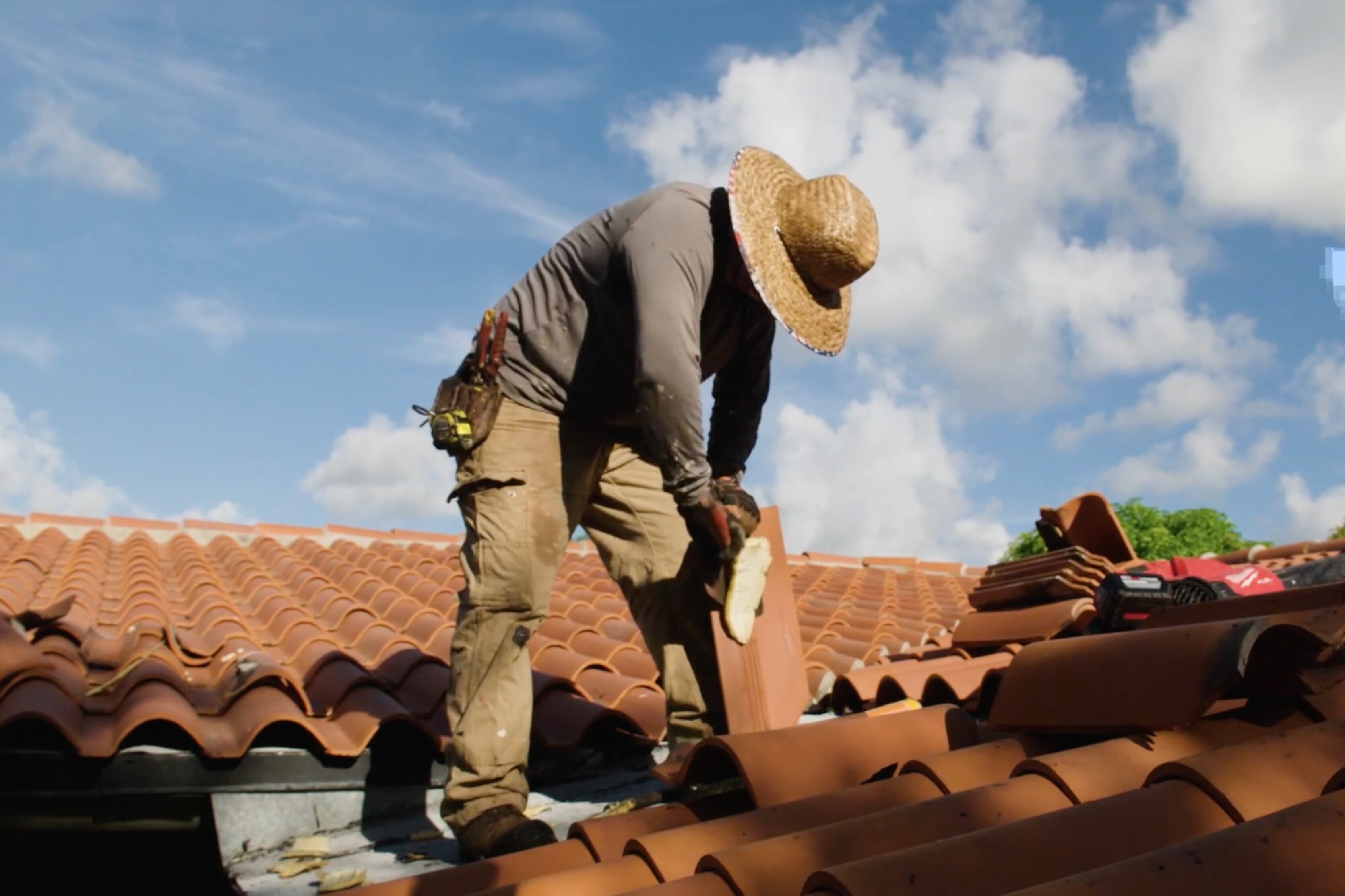 A worker picks up a roof tile on top of a roof.