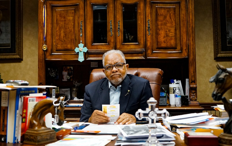 Bishop Ronnie Crudup of New Horizon Church International sits behind a desk.
