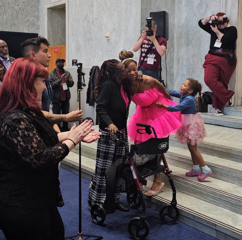 A woman in a bright pink dress hugs an older lady as a little girl reaches out to her from behind.