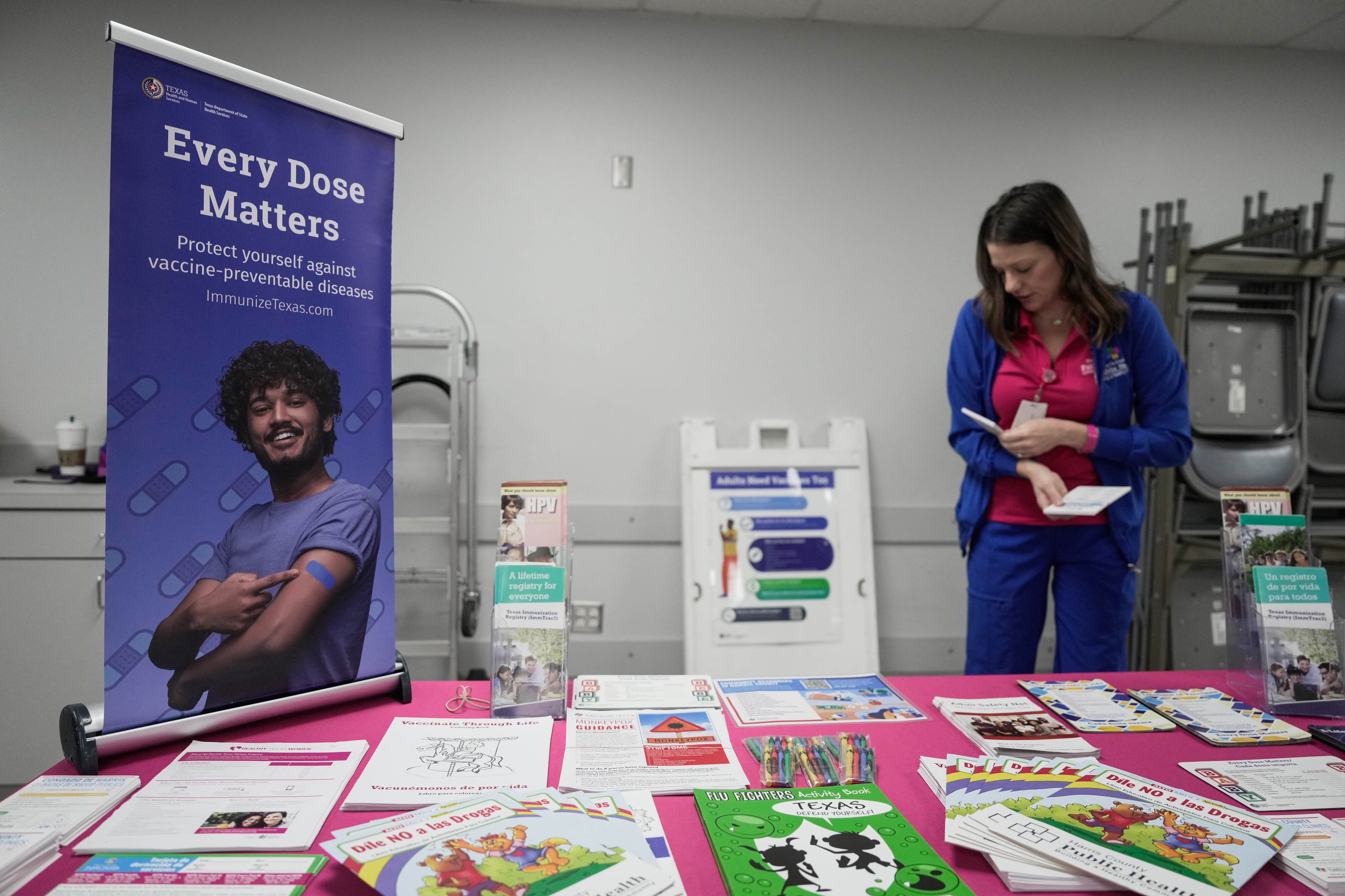 A woman stands at a booth offering information on the measles vaccine.