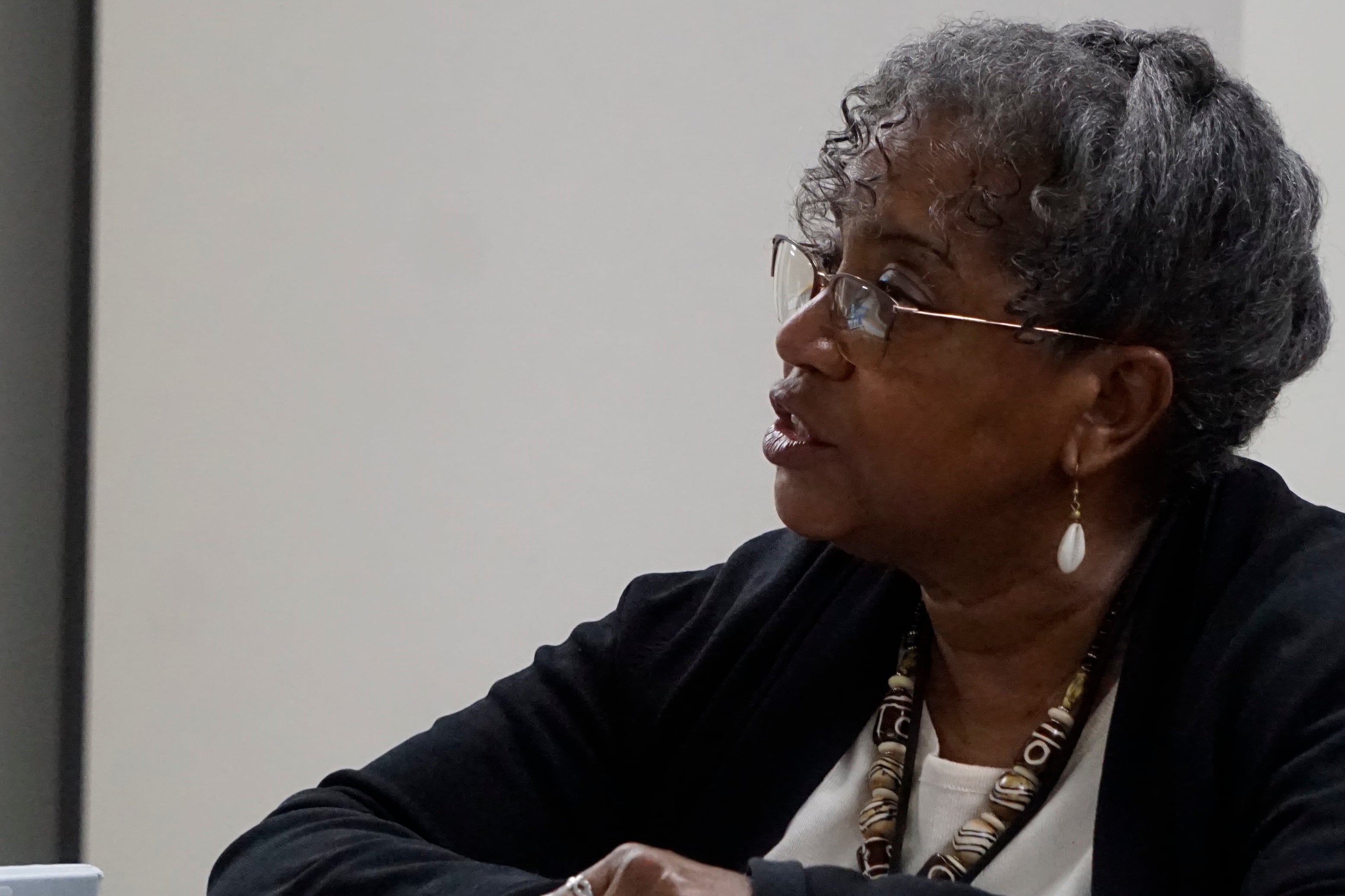 A woman sits behind a table with a binder in front of her and speaks during a meeting.