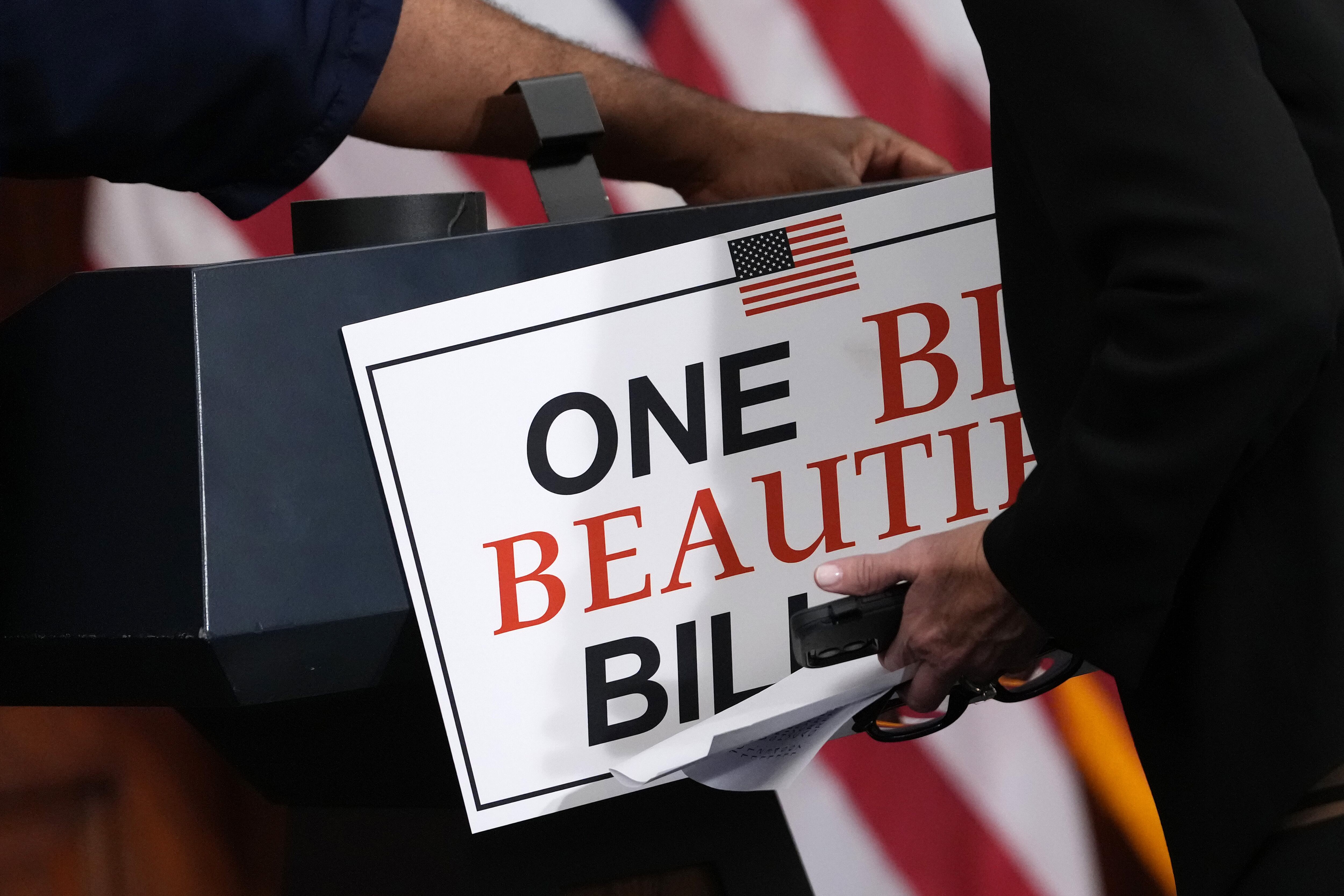 Staffers remove a sign touting the One Big Beautiful Bill from a podium.