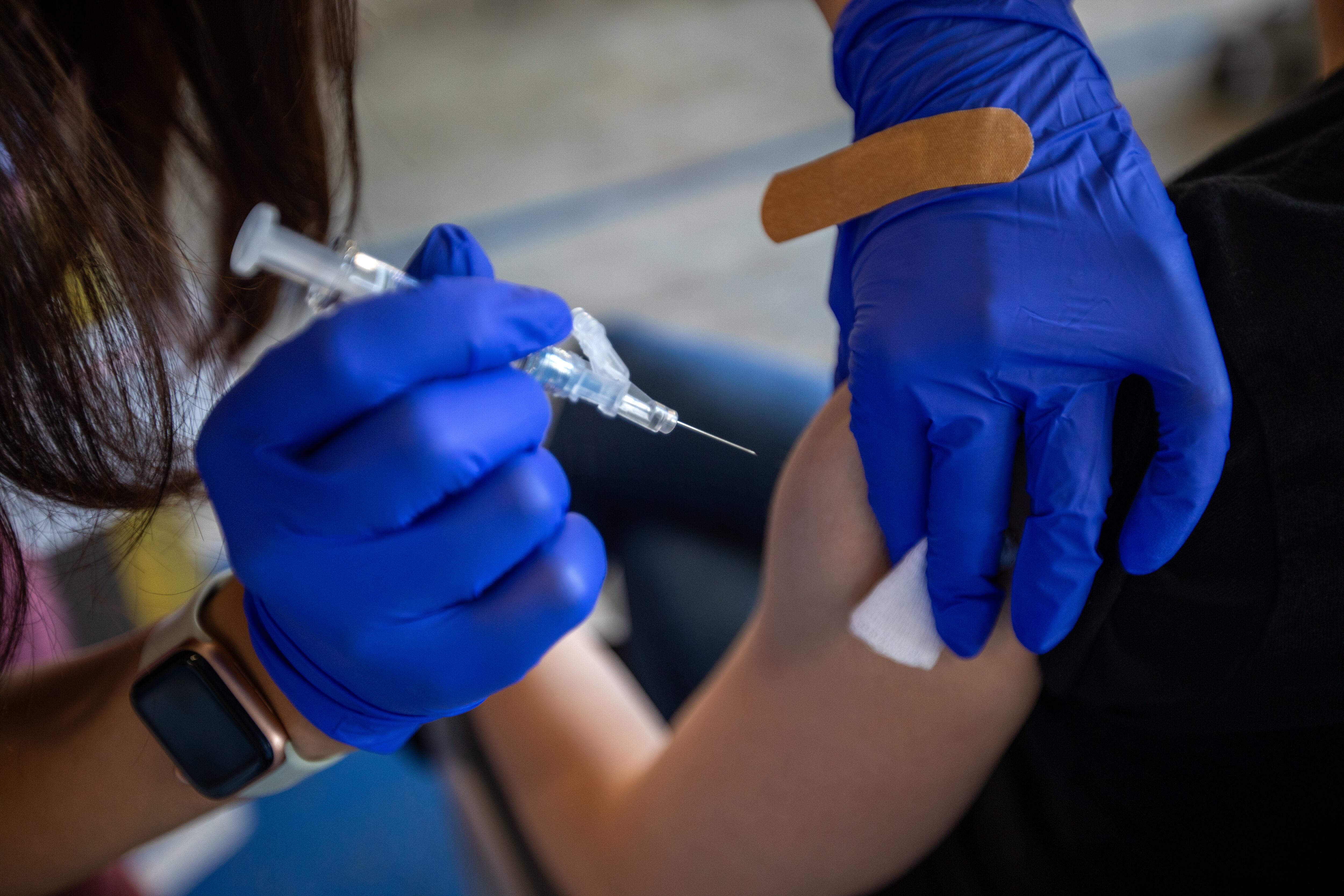 A health care worker wearing blue gloves gives someone a shot in the arm.