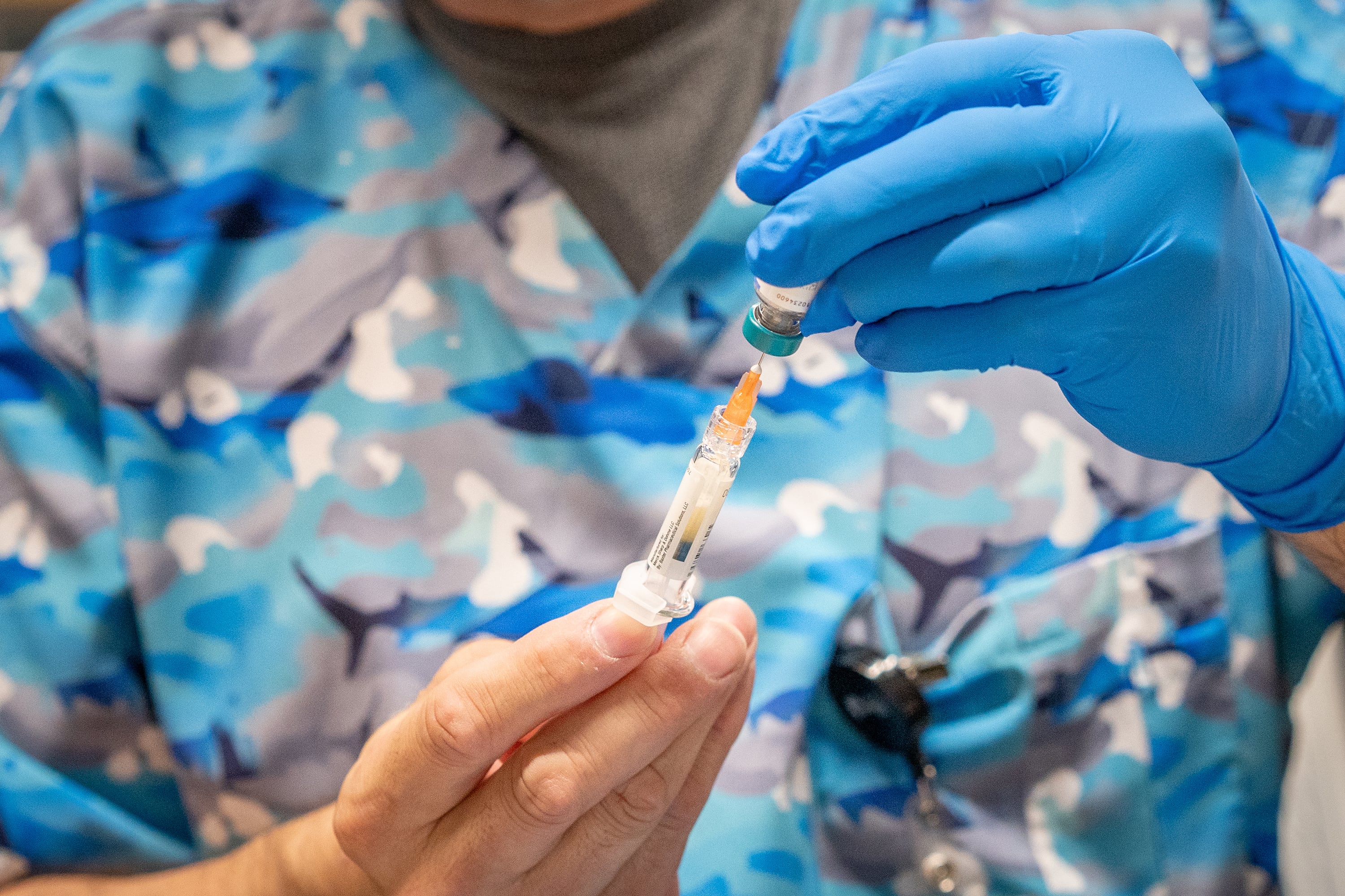 An up-close view of a pair of hands pulling a dose of the MMR vaccine.