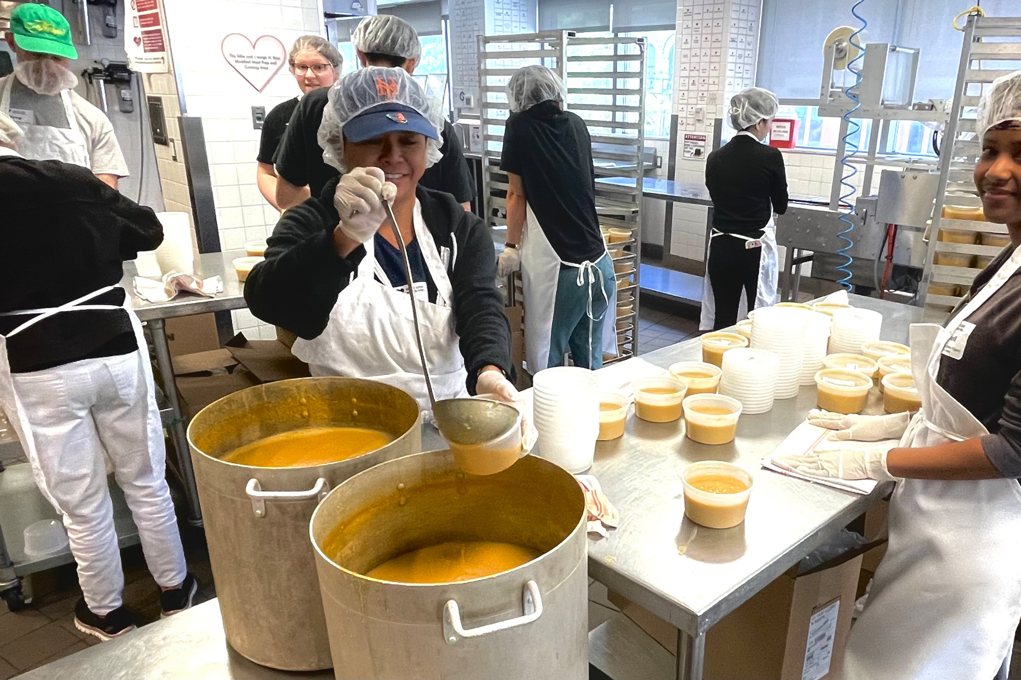 Volunteers ladle soup into containers in a kitchen.