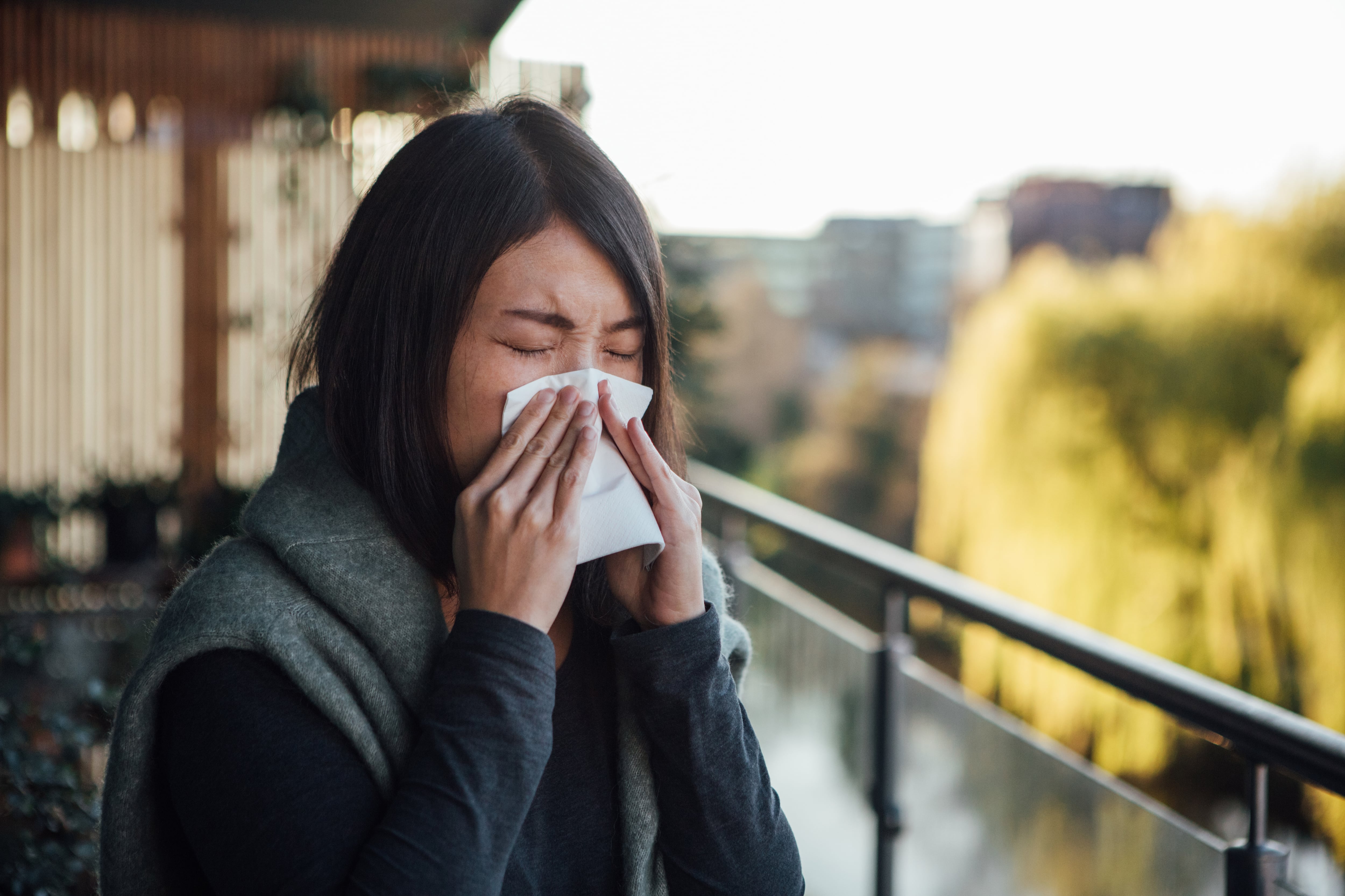 A woman standing on a balcony sneezes.