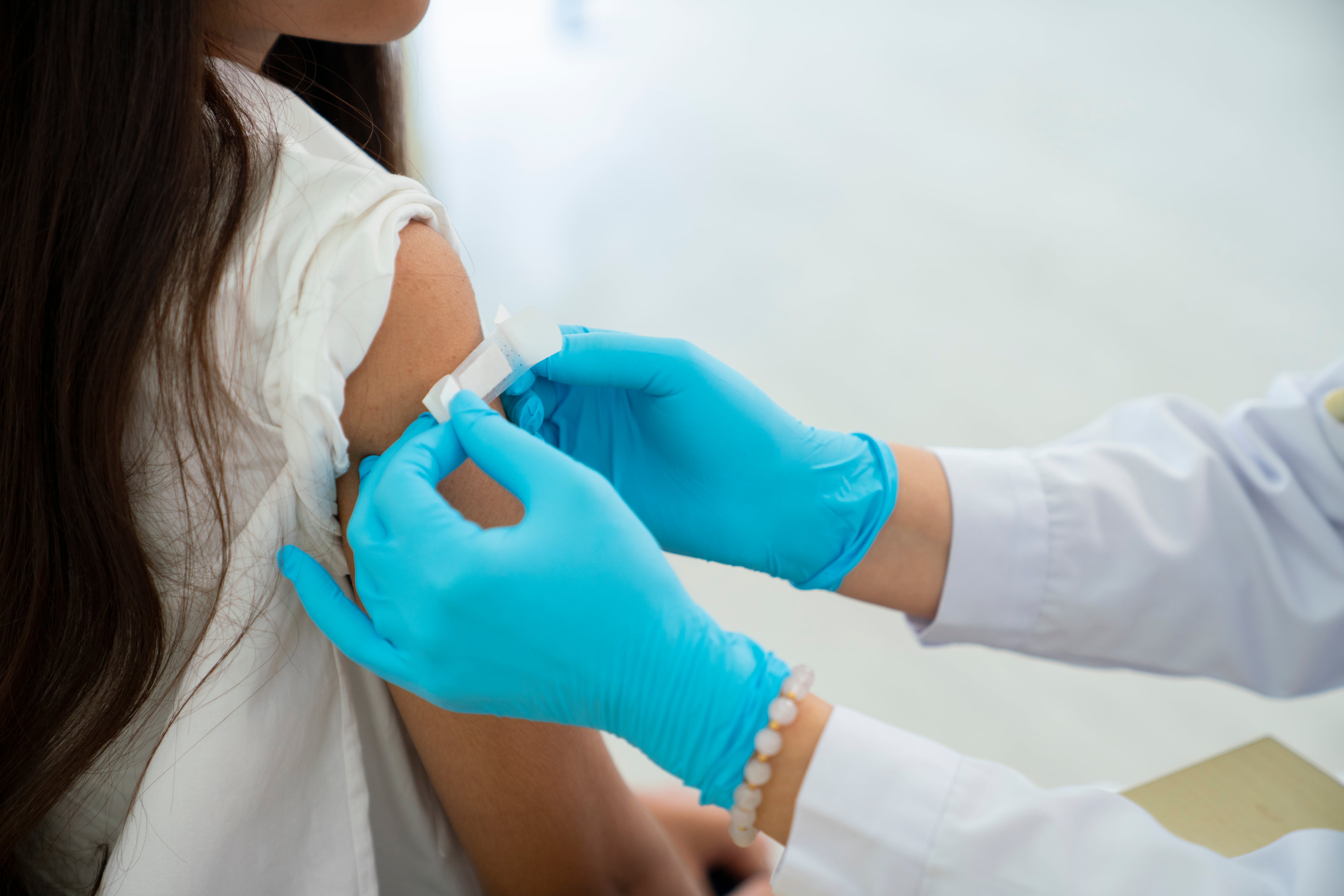 Doctor applies bandage to preteen girl's arm following an immunization.