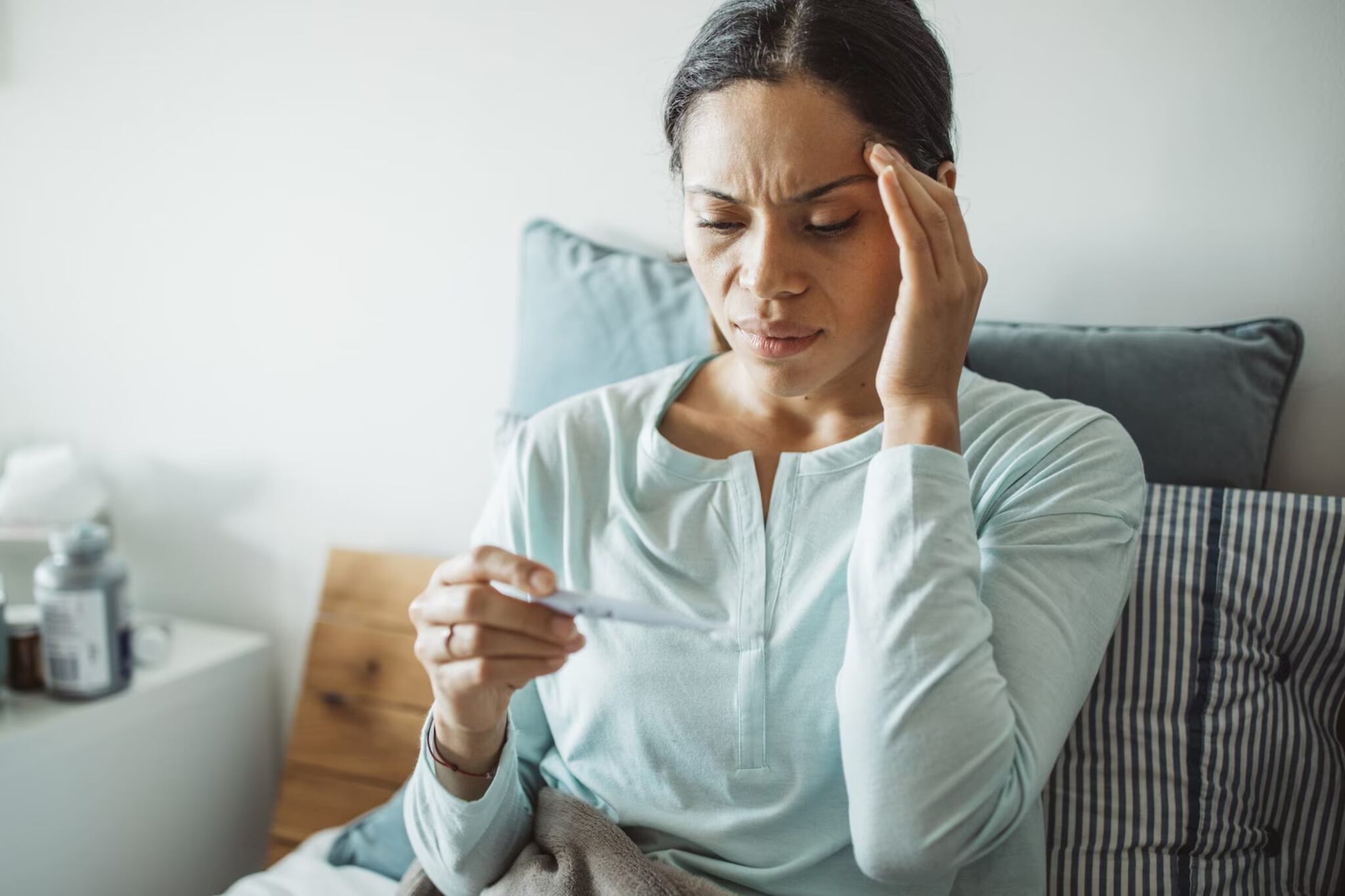 A woman checks the reading on a fever thermometer.