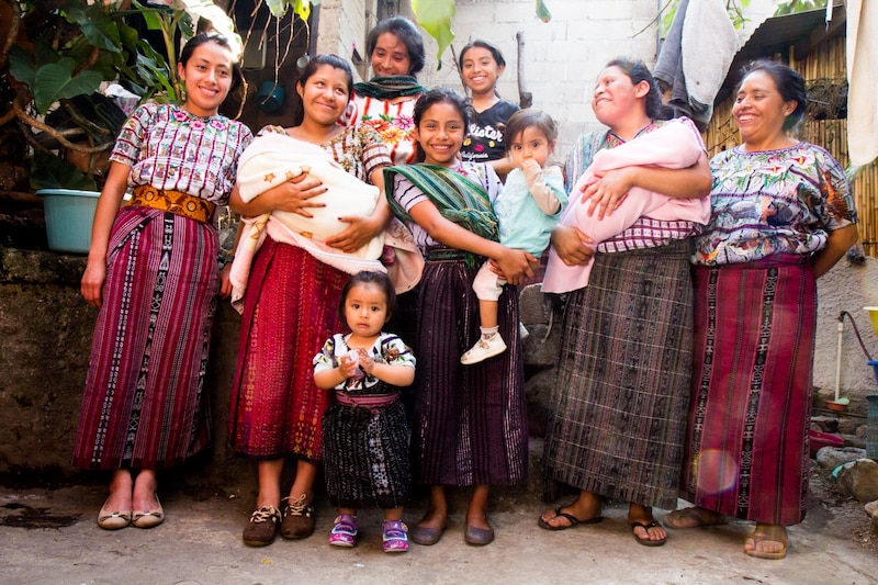A group of women wearing colorful traditional clothing pose for a group photo in Guatemala.
