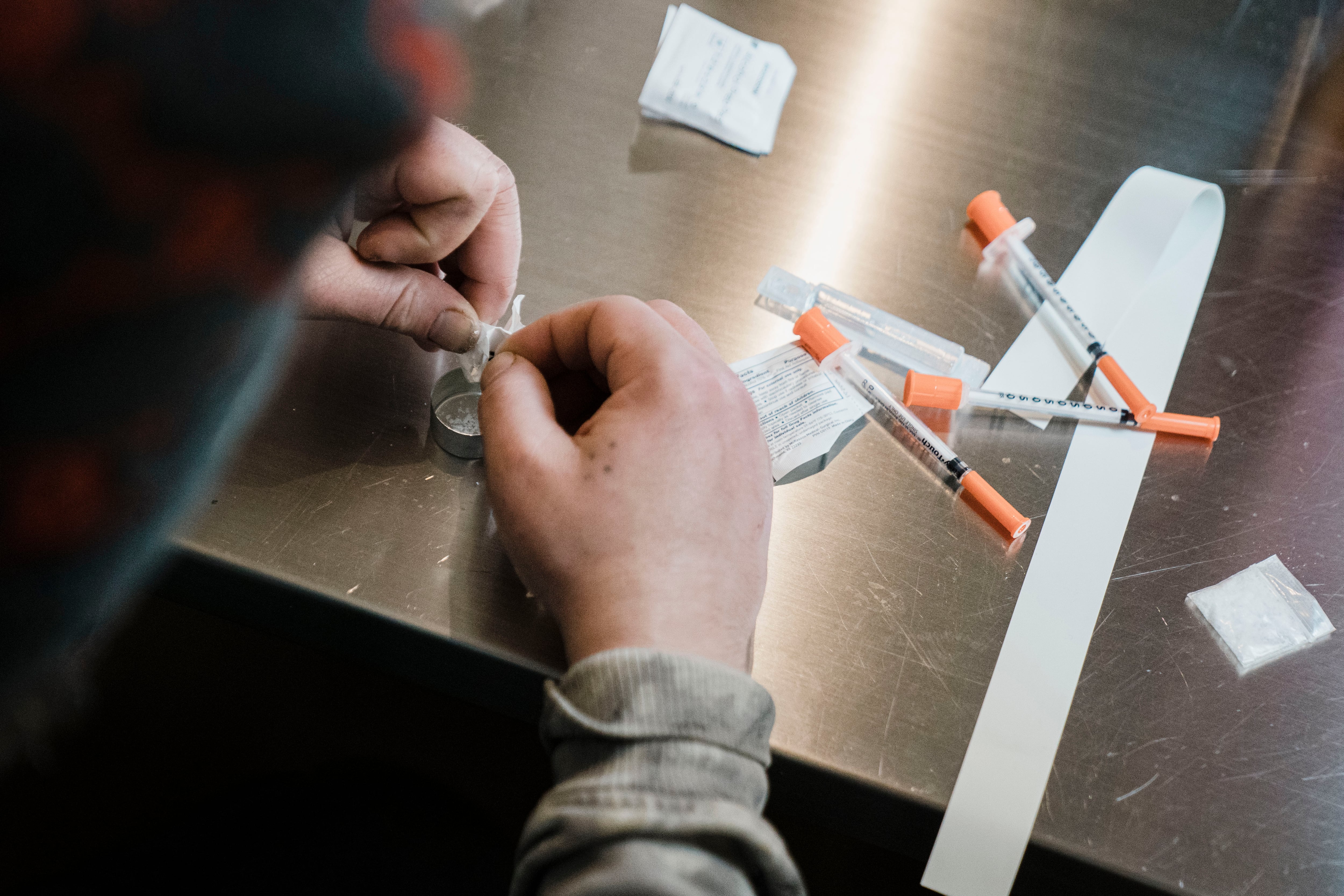 A man utilizes a narcotic consumption booth at a safe injection site, with syringes on a table.