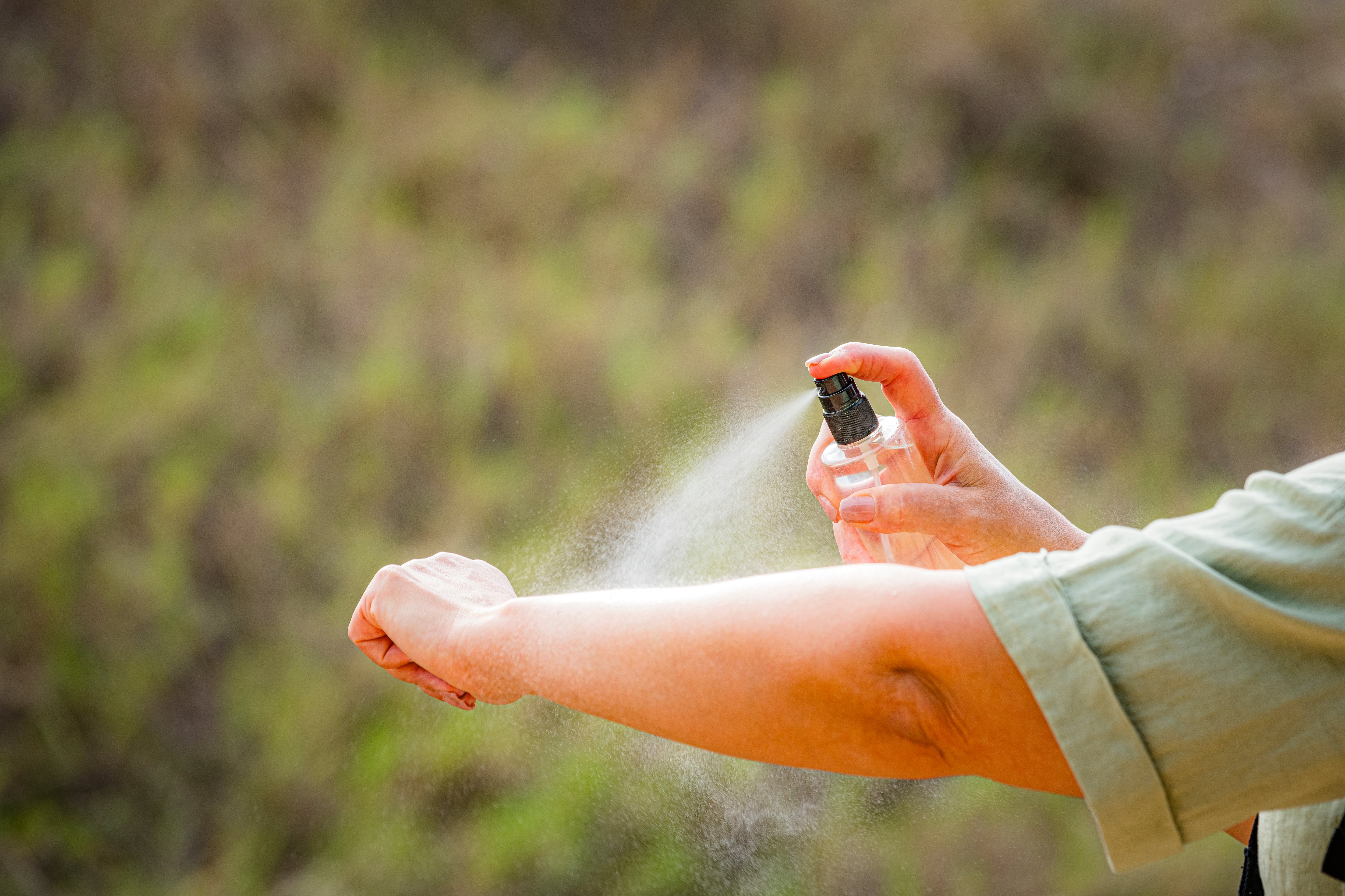 A person sprays insect repellent on their arm.