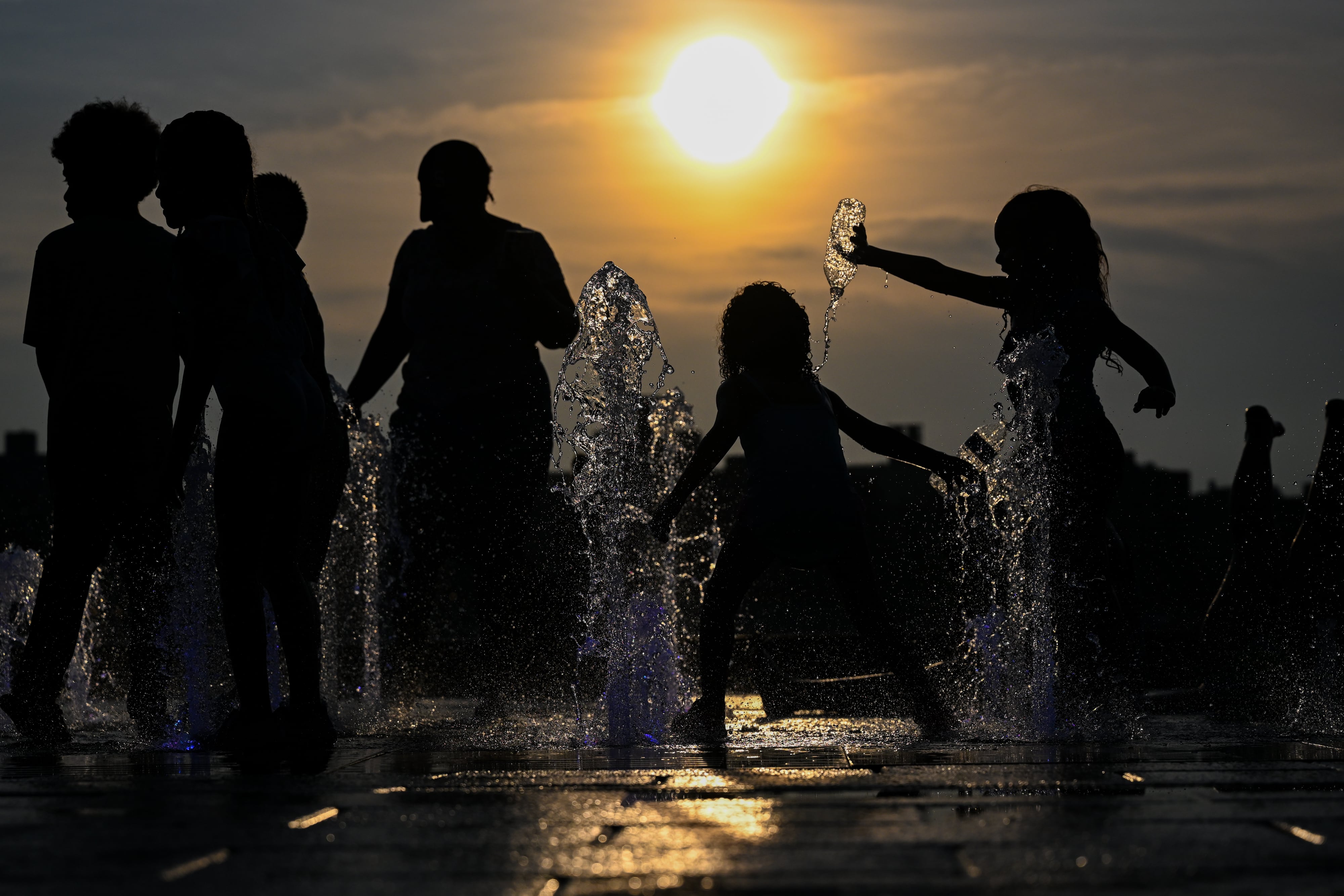 Children play in a fountain under a bright sun.
