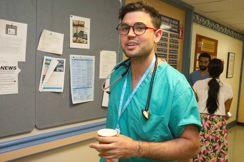 A doctor wearing scrubs stands in a hospital hallway.