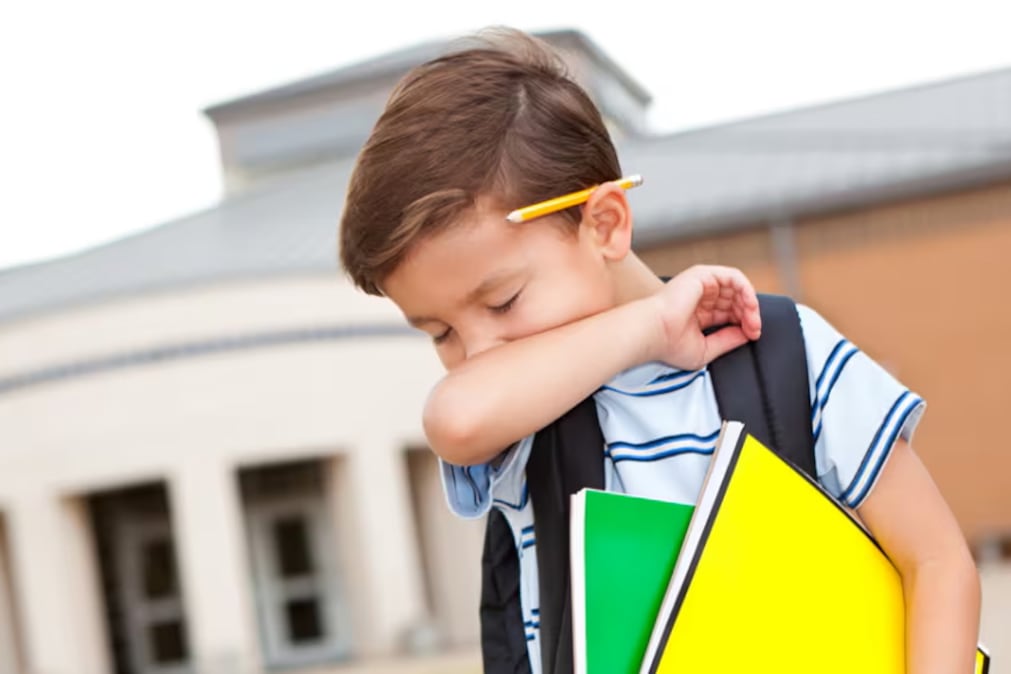 A boy covers his mouth with his arm while he coughs.