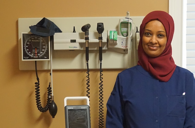 Maha Mousnad stands in front of medical equipment in a health clinic.