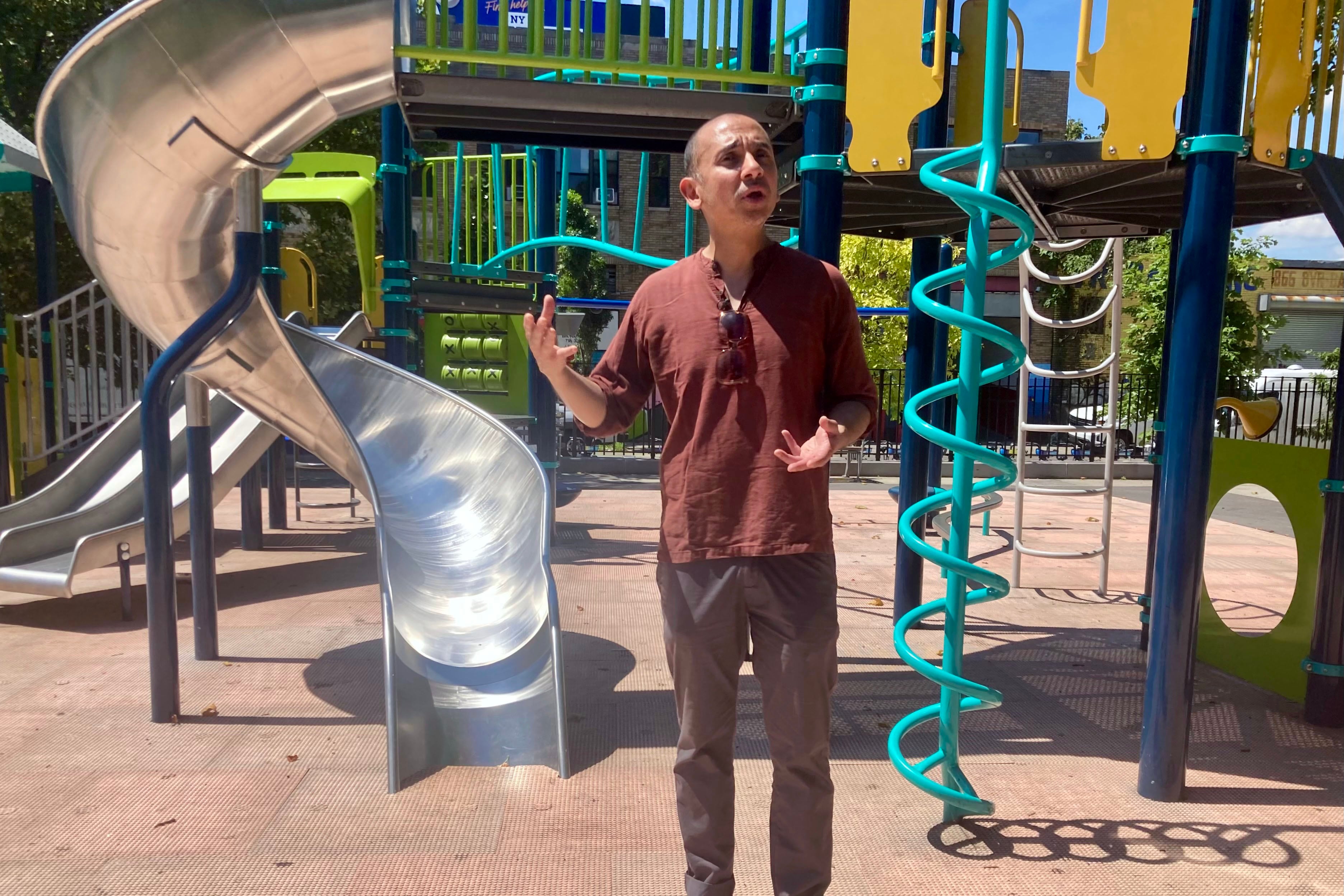 A person wearing a dark red shirt stands in front of an outdoor playground.
