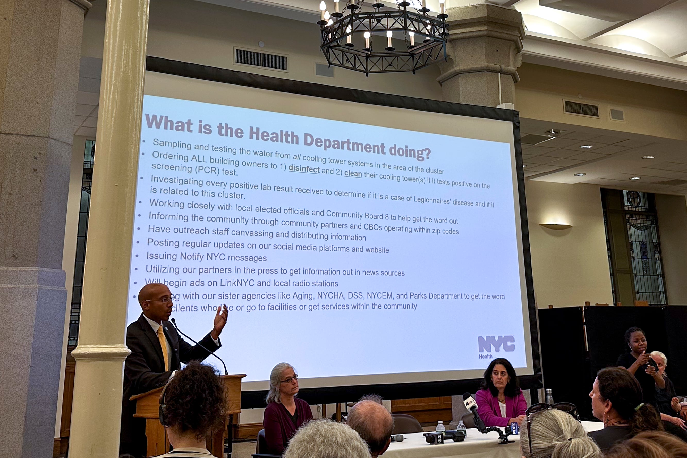 A Black male standing in front of a presentation screening and speaking to the crowd.