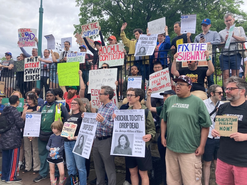 Protesters stand and hold signs condemning a decision to pause a congestion pricing plan.
