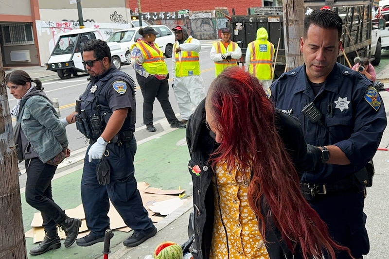 Two police officers arrest two homeless women on the street.
