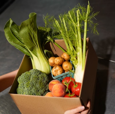 A box of produce includes broccoli, potatoes, tomatoes and greens.