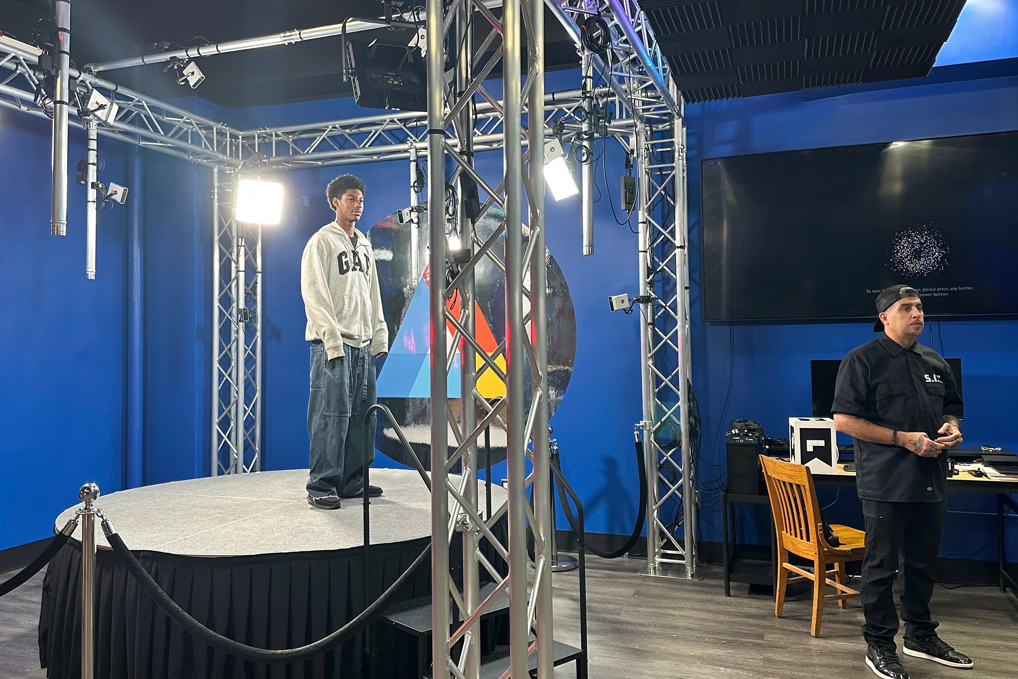 A high school student stands on a platform while an adult stands on the ground in a high school studio.