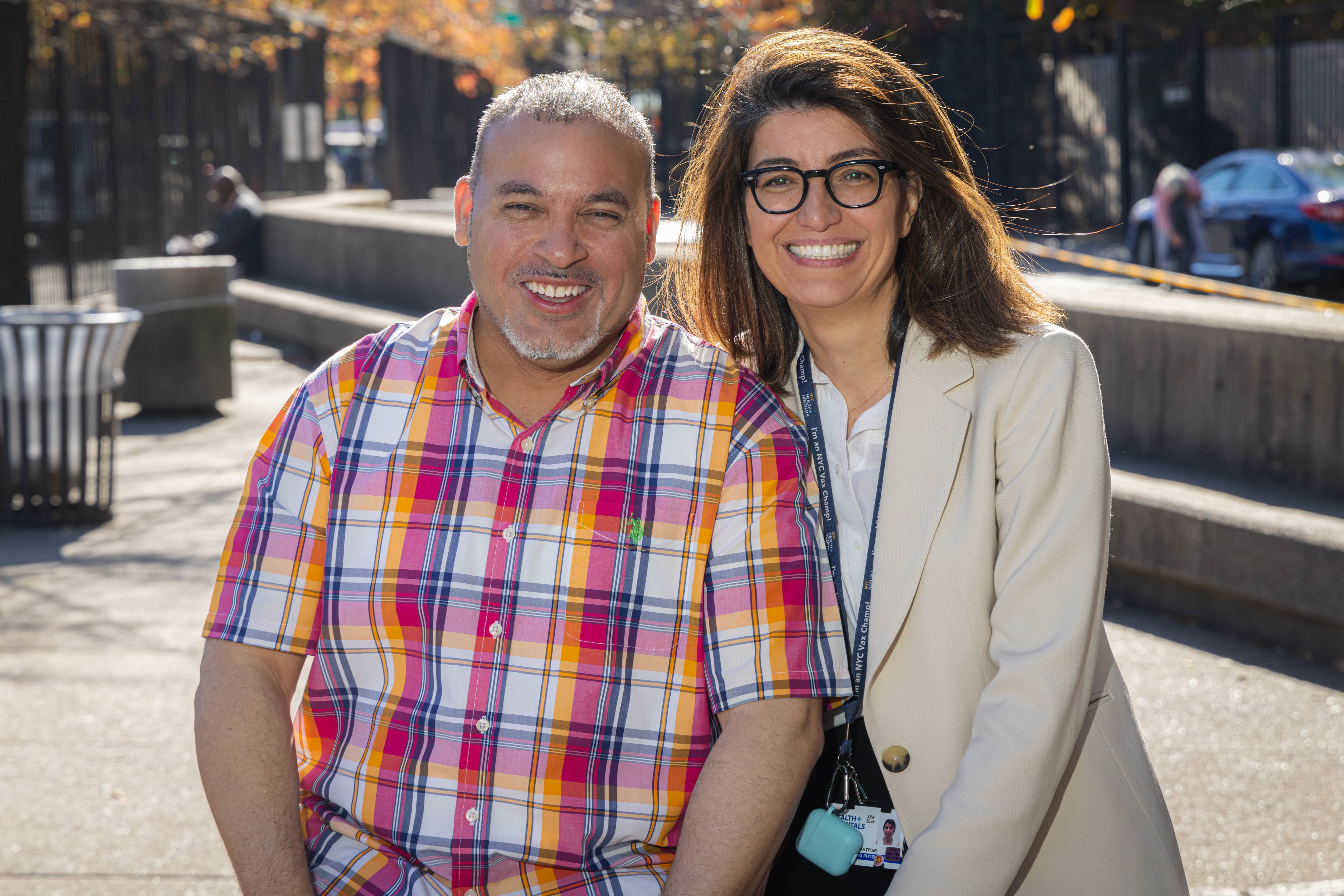 A male patient smiles for a photo with his doctor in an outdoor setting.