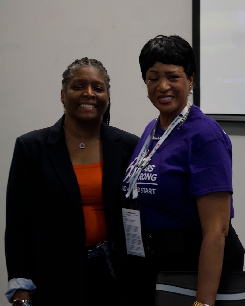 Two women stand together in front of a neutral backdrop.
